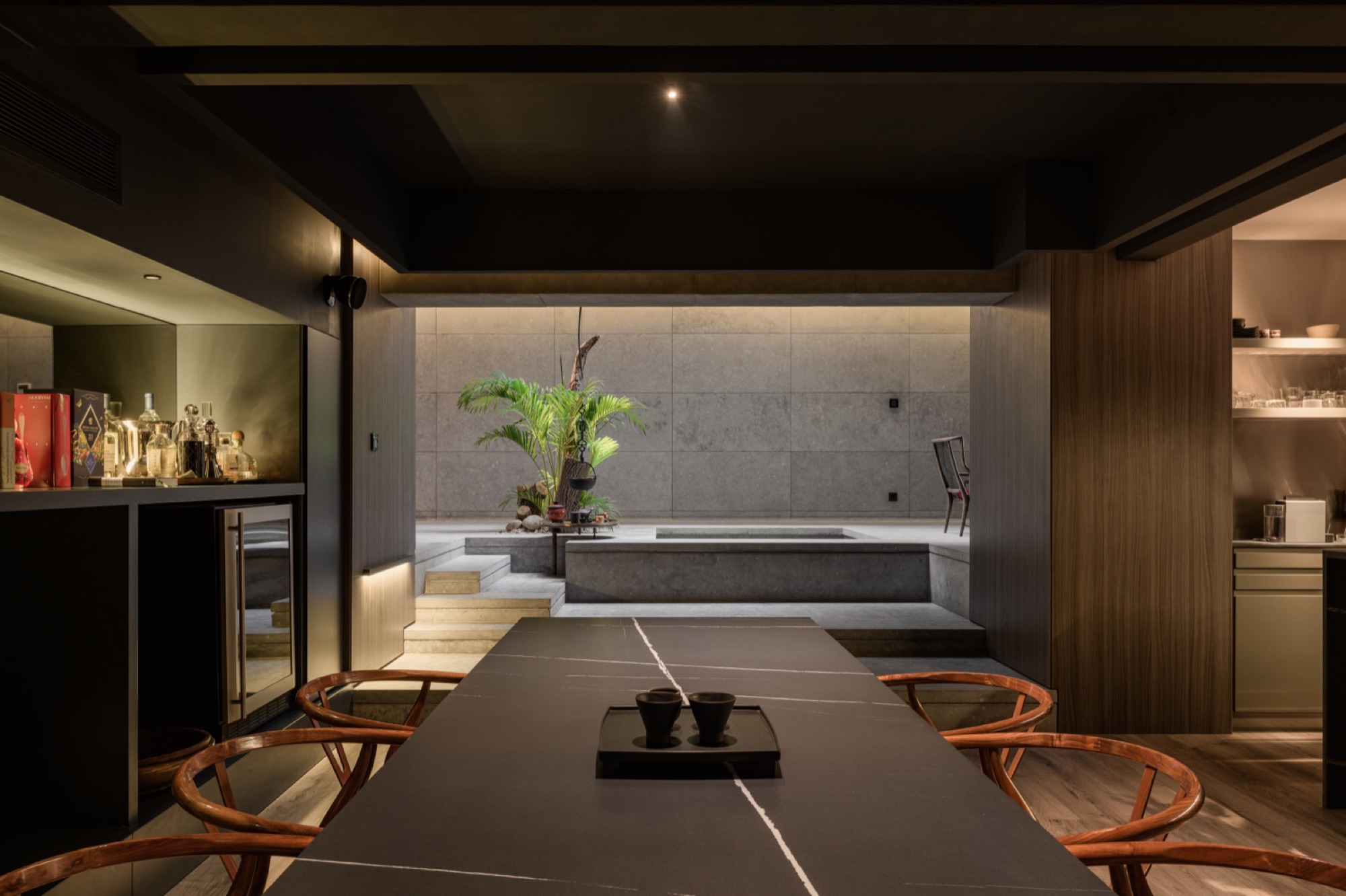 A long dining room in stone and dark wood, the table laid with black vessels