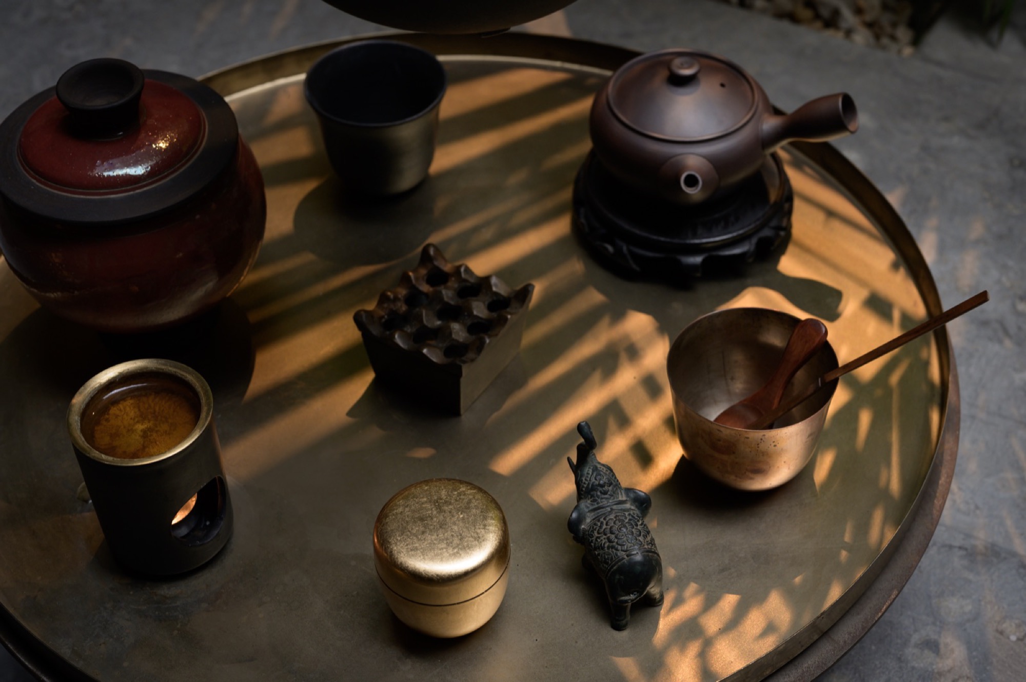 A round copper tray of small vessels in dappled afternoon light
